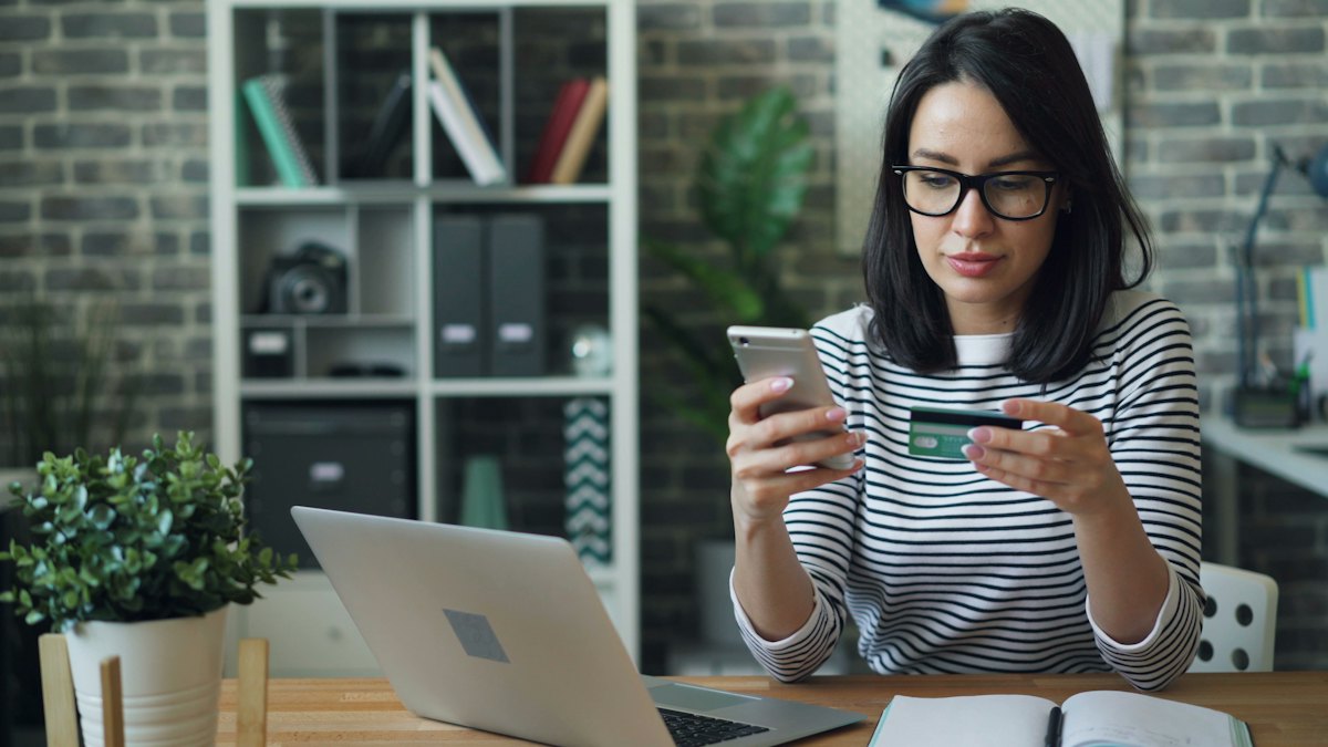 Mulher olhando o celular com cartão de crédito na mão